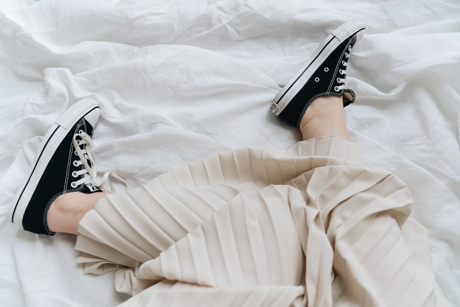A casual outfit with a pleated skirt paired with black sneakers on a white sheet.