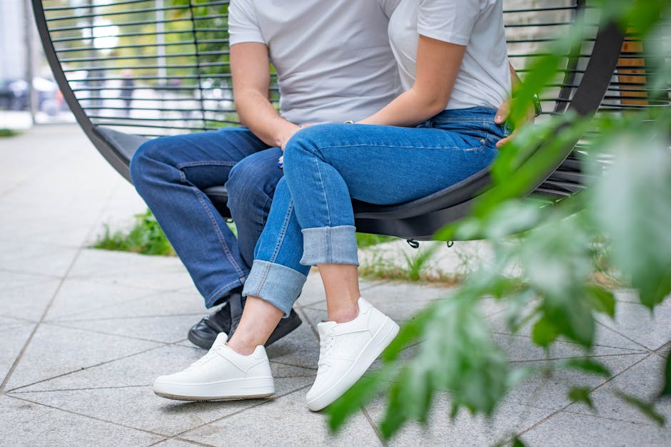 A couple in jeans and sneakers casually sitting on a modern swing outdoors.