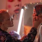 A makeup artist applying cosmetics to a woman in a warmly lit studio, creating a vibrant look.
