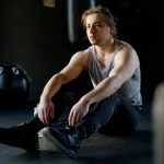 A male athlete rests after a workout session, sitting on the gym floor in calm reflection.