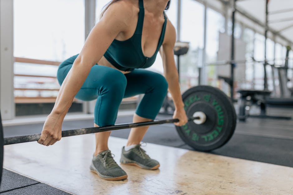 A woman in activewear lifting a barbell in a gym, showcasing strength and fitness focus.