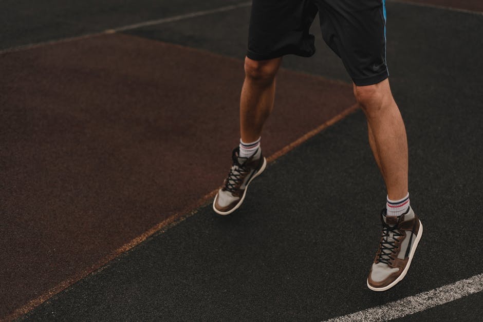 Close-up of an athlete's legs and sneakers on an outdoor basketball court.