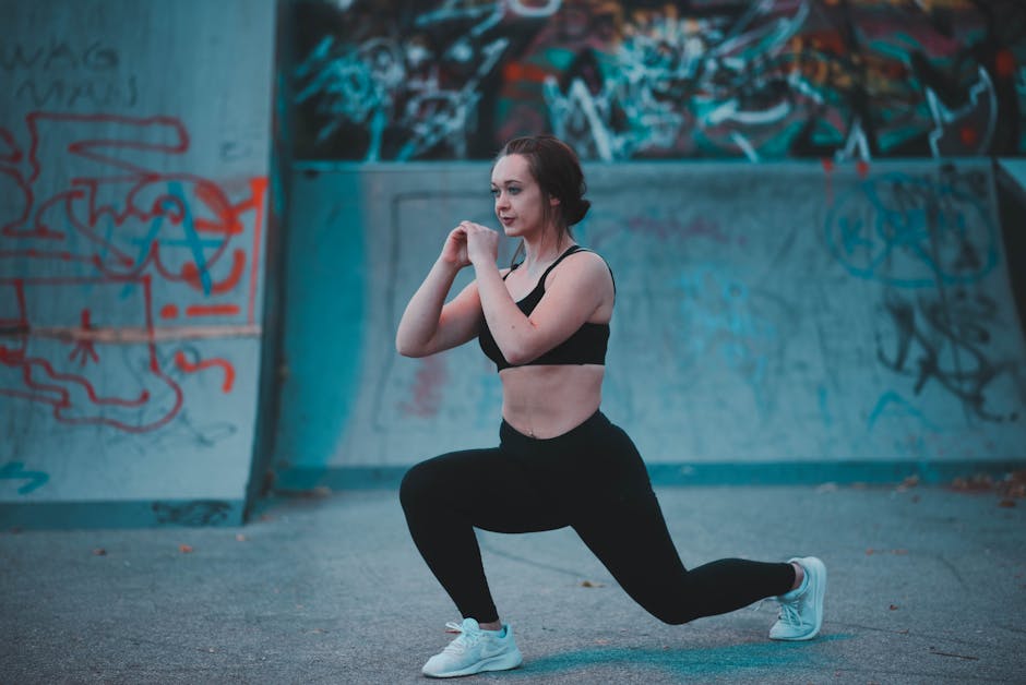 Confident woman in activewear performing lunges in an urban skate park with graffiti backdrop.