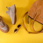 Stylish brown handbag, fashionable eyewear, and sport shoes on vibrant yellow background.