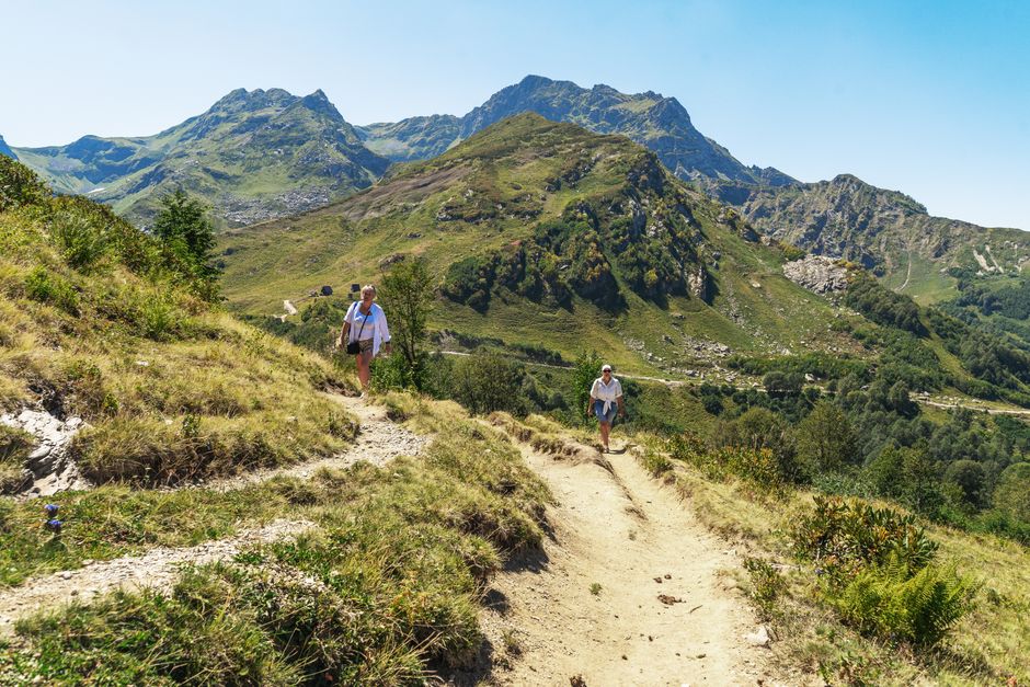 Two hikers walking along a trail amidst beautiful mountainous scenery on a sunny day.