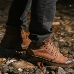 Crop anonymous person in brown boots and black jeans walking on stones near river bank