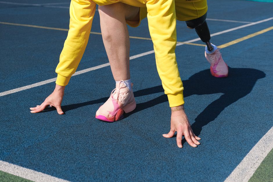 Female athlete with a prosthetic leg preparing to run on an outdoor track.