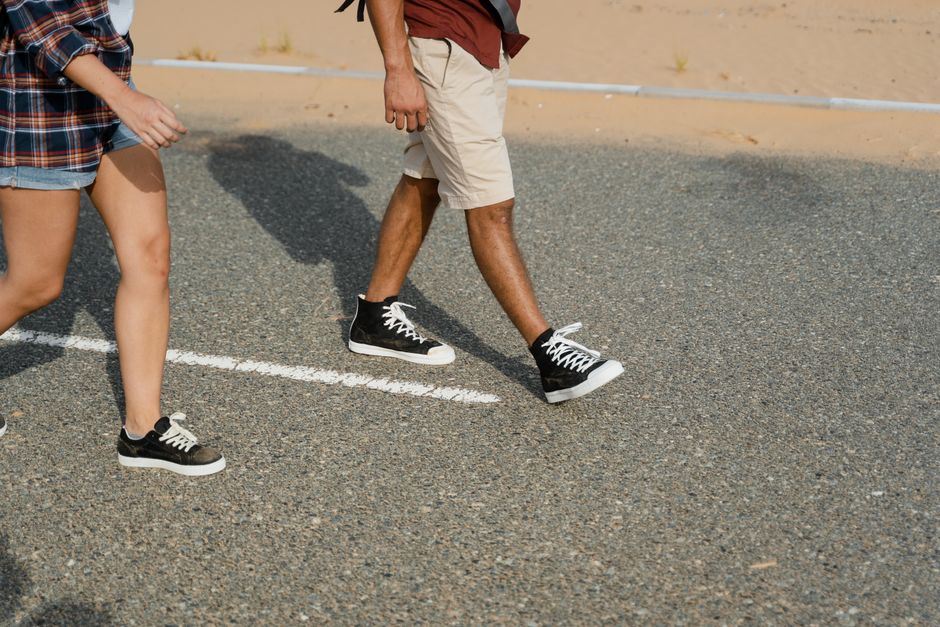Close-up of two people in sneakers walking down a desert road.