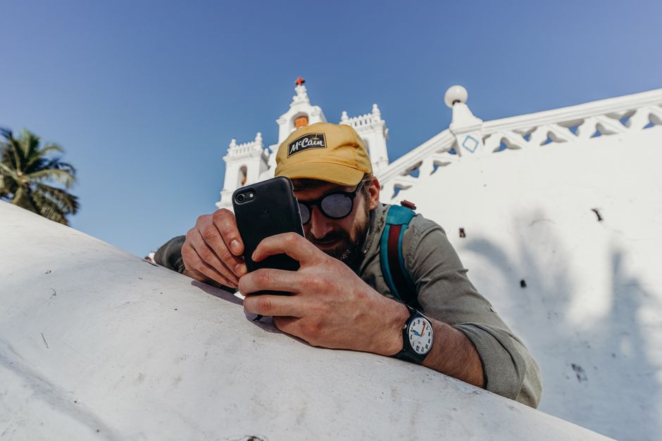 A man photographs a white church in Goa, India, under bright sunshine, blending travel and architecture.