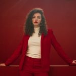 Elegant woman in a stylish red suit posing confidently in front of a matching red background.