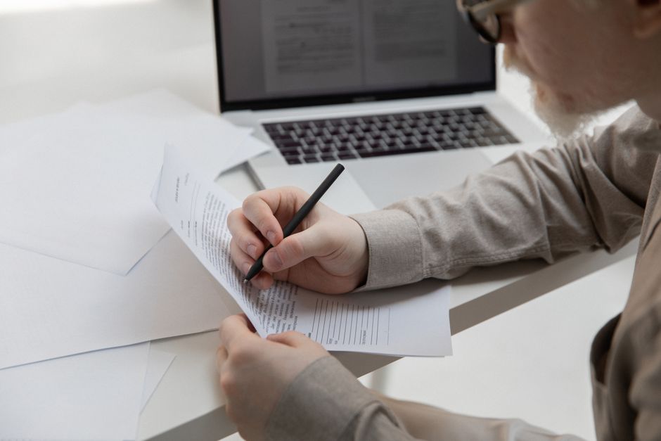 Side view of crop anonymous manager with pen watching paper with text near netbook on desk