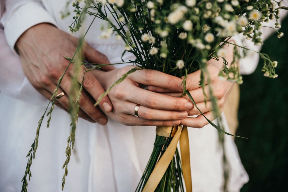 Romantic close-up of couple's hands holding a wedding bouquet, symbolizing love and commitment.