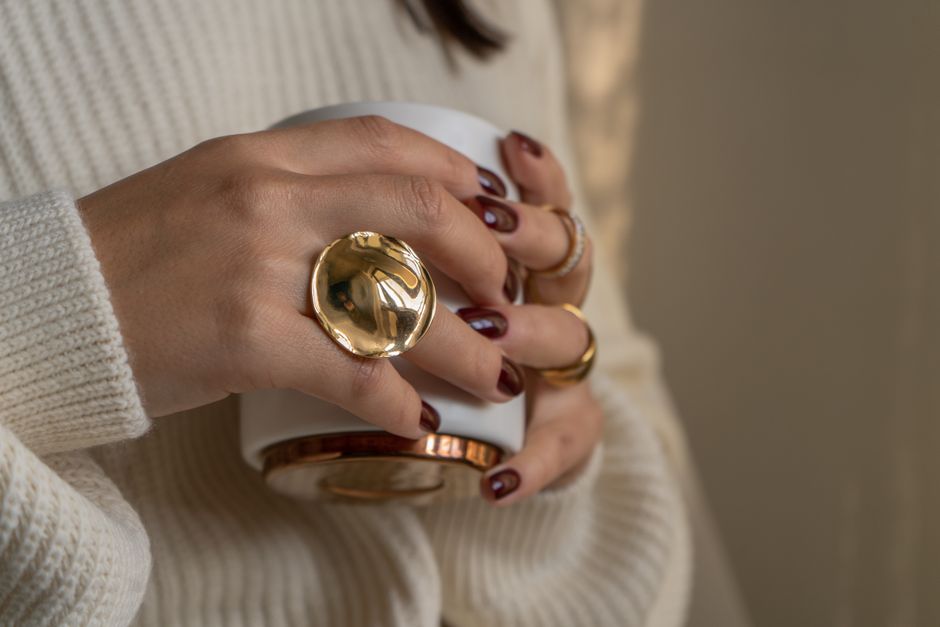 Close-up of a woman's hands holding a mug, adorned with gold jewelry, cozy and warm setting.