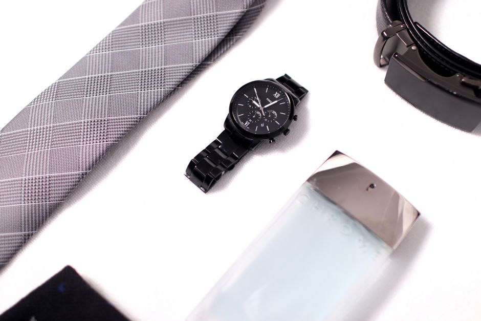Flat lay of men's fashion items including a watch, tie, belt, and cologne.
