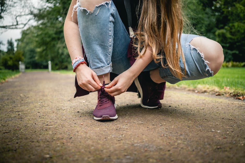 Close-up of a young woman tying purple sneakers on a path in a park, denim style.