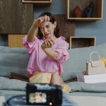 Woman in pink blouse displaying colorful jewelry for vlogging indoors.