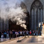 Smoke rises during a ceremony in a grand Gothic cathedral with gathered attendees.
