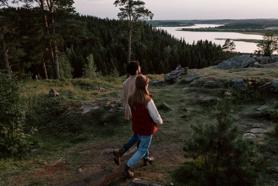 A couple explores a tranquil forest with a scenic river view, encapsulating nature's peaceful beauty.