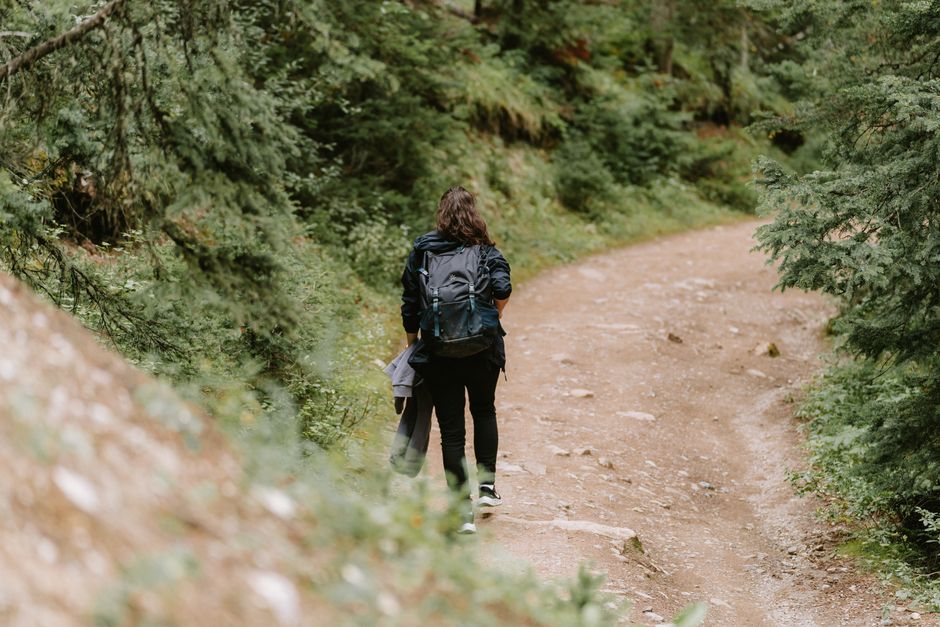 A woman hiking with a backpack on a scenic dirt road in Banff, surrounded by lush trees.