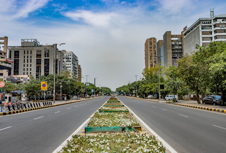 A vibrant urban scene in New Delhi, showcasing modern architecture and a wide, empty road.